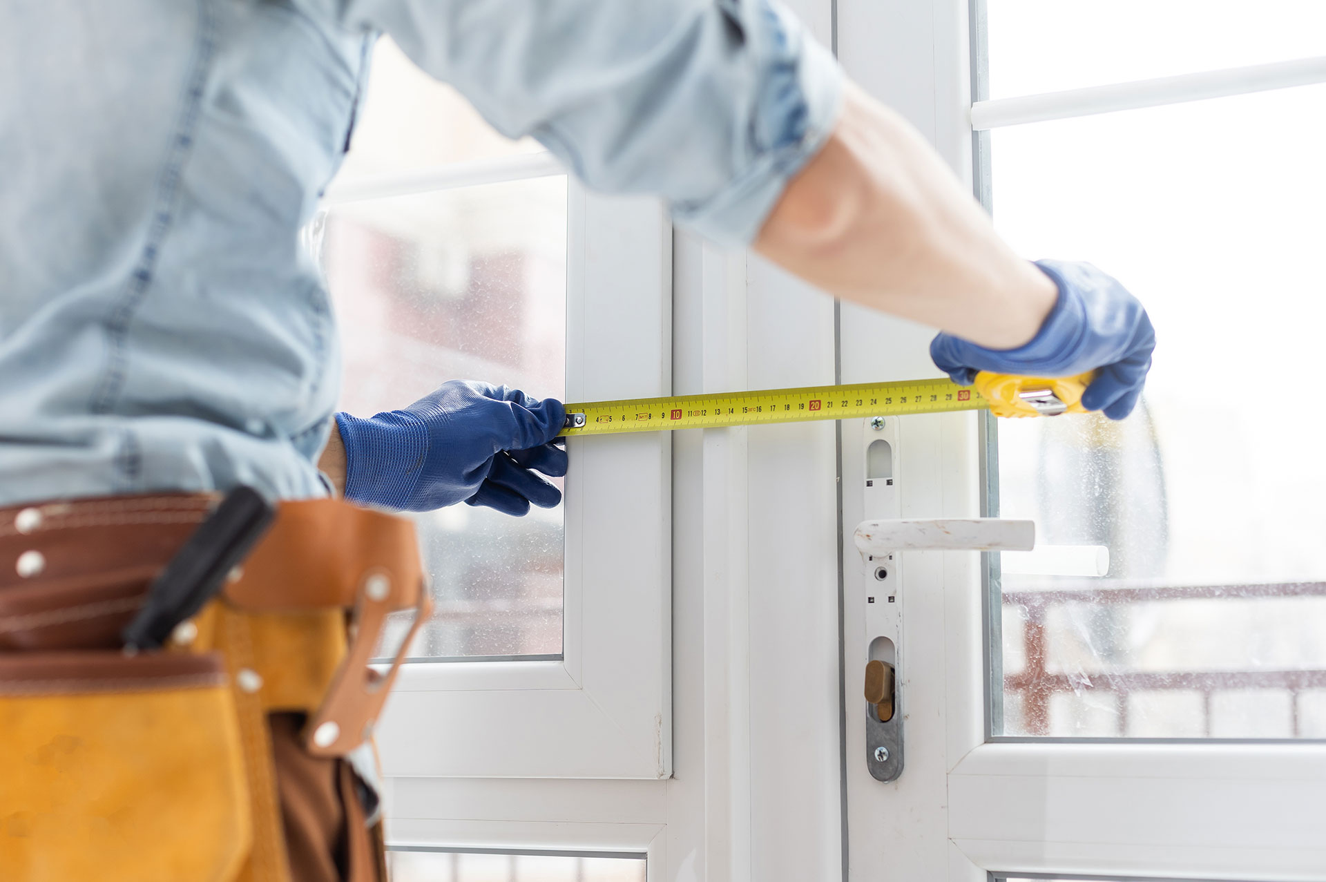 A person measuring a window with a tape measure while wearing gloves and standing outside.