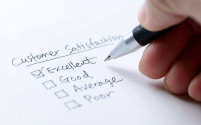 The image shows a hand holding a pen over a piece of paper with the words  customer satisfaction  written on it, accompanied by a list of criteria such as  excellent,   good,   average,   poor,  and  very poor.