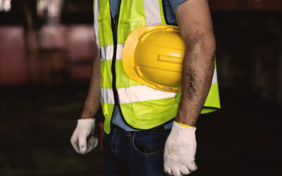 The image shows a construction worker wearing a high-visibility vest with reflective stripes, holding a clipboard and standing outdoors at night.